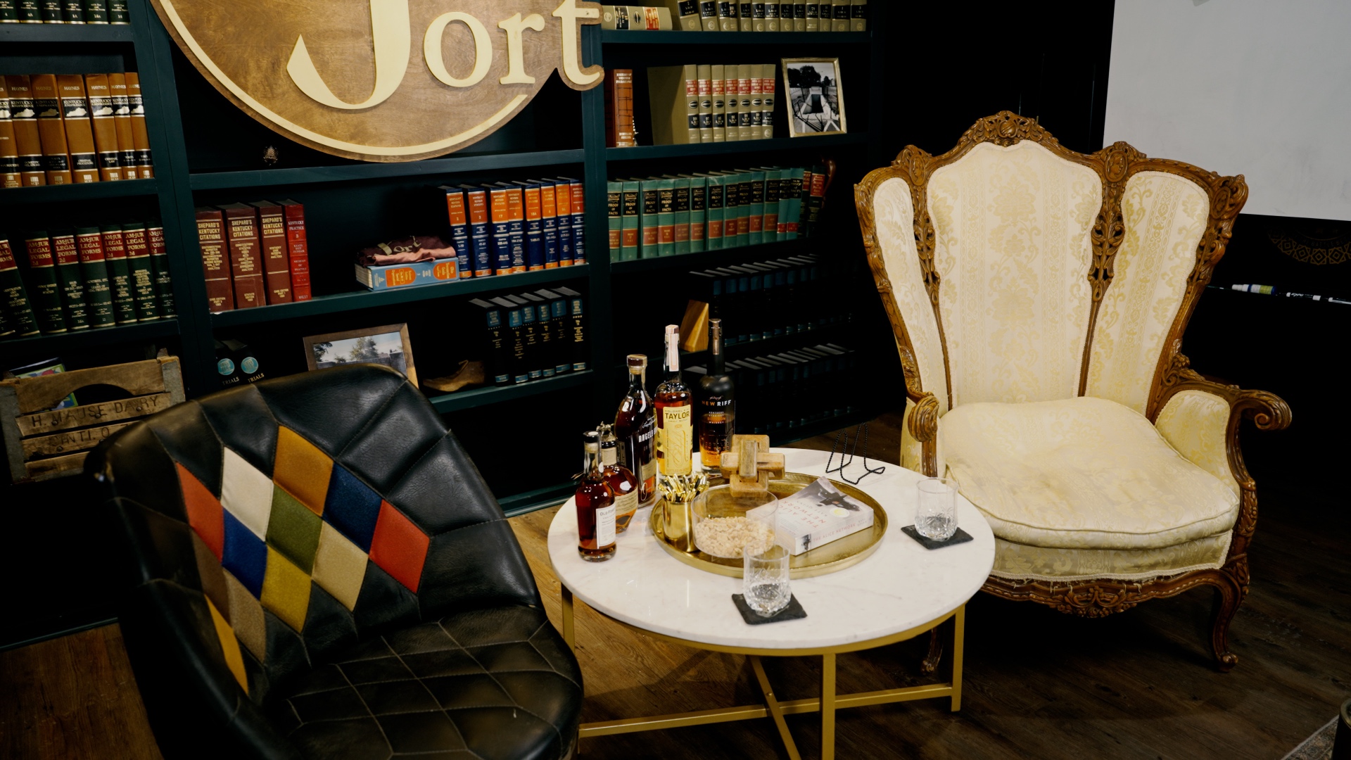A bourbon spread on a marble side table — bottles, crystal rocks glasses, and ice beside the carved armchair at The Fort